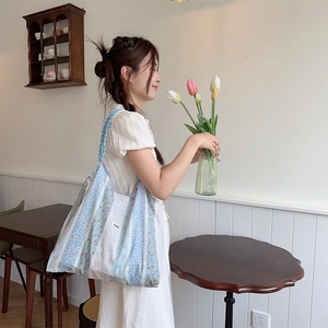 Close-up of a blue and pink floral canvas tote bag held by a model in a cozy room