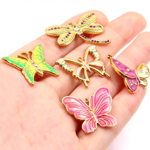 Colorful enamel butterfly and dragonfly charms with rhinestones held in a hand