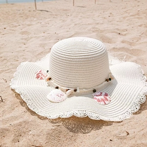 Close-up of white straw sun hat with shell decorations on a sunny sandy beach