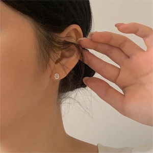 Close-up of geometric square silver stud earrings with sparkling zircon on ear