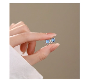 Macro shot of minimalist silver earring with blue zircon stone held by fingertips