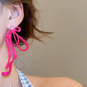 Close-up of a model wearing bright magenta ribbon bow earrings with sparkling white crystals