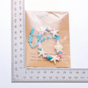 Macro detail of bead bracelet with starfish and turtle charms next to a ruler for size