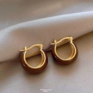 Detail of brown and gold enamel hoop earrings on elegant champagne silk fabric background