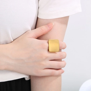 Close-up of a large square titanium steel ring with a golden matte finish worn on a finger