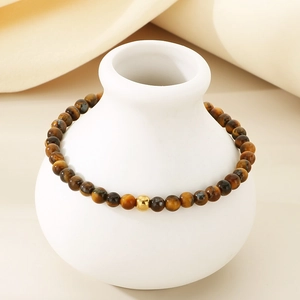 Detail of tiger eye bead bracelet with gold accent bead on white ceramic vase