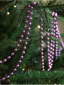 Close-up of purple beaded garland hanging on a Christmas tree with warm glowing lights