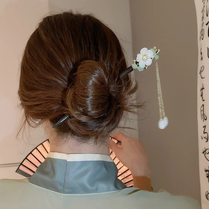 Detailed close-up of a white magnolia hair pin with golden tassels on black wood