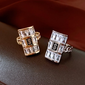 Dettaglio macro di anelli oro e argento con zirconi rettangolari e decoro lettera S