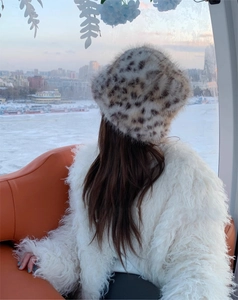 Winter leopard print faux fur bucket hat worn by a woman in a snowy city landscape scene