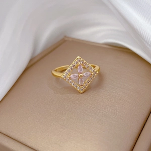 Close-up of golden square flower ring with pink gemstones on white silk background