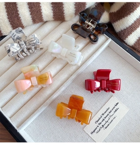 Detailed close-up of six colorful acetate bow hair claws on a cream velvet tray