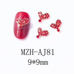 Détail de bijoux d'ongles cœur rouge 9x9mm avec base dorée sur un faux ongle rouge