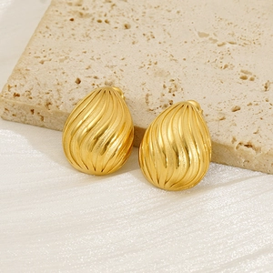 Detailed macro of gold geometric teardrop earrings with spiral texture on stone surface