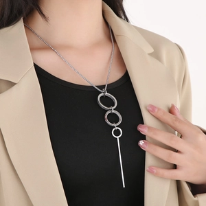 Detail of silver geometric multi-ring long pendant necklace on a beige blazer background