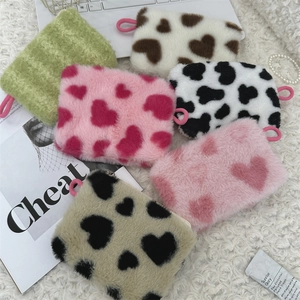 Plush heart and cow print mini pouches displayed on soft white wool texture background