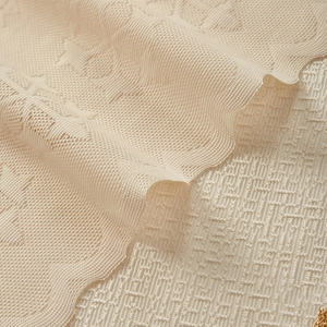 Macro shot of beige lace curtain fabric with floral embroidery and wavy edges