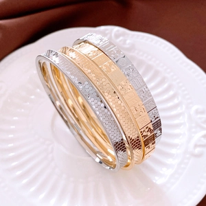 Detail of four gold and silver textured metal bangles featuring intricate engraved patterns
