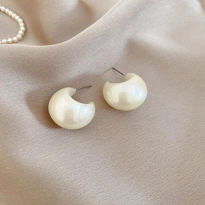 Detail of C-shaped champagne acrylic earrings with pearl luster on silk fabric