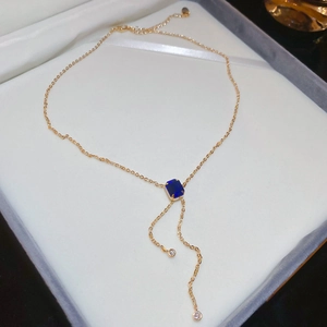 Detailed macro of gold tassel necklace featuring a square blue gemstone pendant
