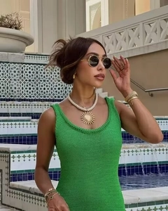 Détail de la robe en tricot vert avec collier soleil doré et bracelet trèfle