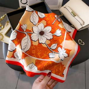 Detailed shot of a floral orange silk scarf with elegant white blossoms and red edges