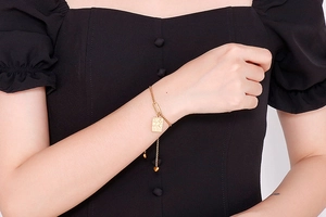 Detailed view of adjustable gold-tone bracelet with engraved square pendant on wrist