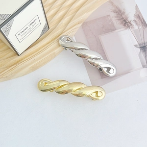 Polished gold and silver geometric spring clips with twist texture on a wooden tray