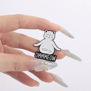 Close-up of white enamel yoga cat pin with OMMMEOW text on hand-held display
