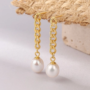 Elegant gold chain earrings with white pearl pendants displayed on a textured stone base