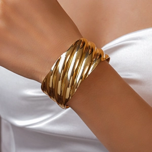 Macro detail of gold textured wavy metal cuff bracelet worn on female model wrist