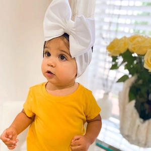 Close-up of baby girl wearing a wide white elastic headband with a large fabric bow