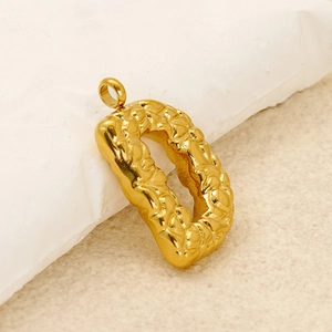 Macro shot of gold letter D pendant with textured hammered surface on a beige base