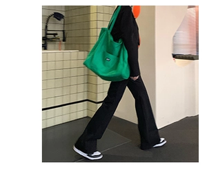 Close-up of a green canvas tote bag with white label worn by a model in a modern setting