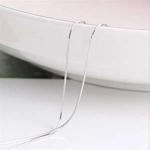 Macro shot of a 1mm silver-plated snake bone chain resting on a white ceramic bowl edge