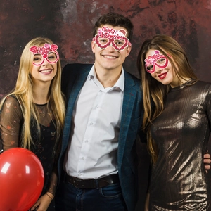 Three people wearing colorful Valentine's Day party glasses with heart and rose designs