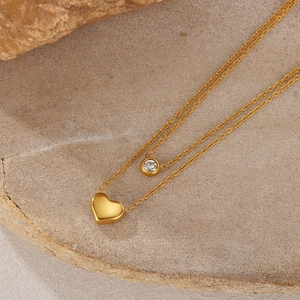 Close-up of double-layer gold necklace with heart and zircon pendants on stone