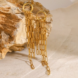 Détail de boucles d'oreilles à pompons dorés avec plusieurs maillons sur une pierre