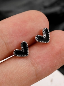 Primer plano de pendientes de corazón plateados con centro negro entre los dedos