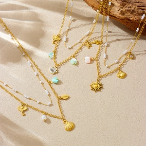 Double-layered gold necklace with sea shell star and pearl charms on sandy background