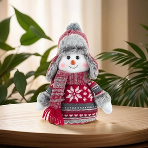 Knitted snowman Christmas ornament figurine on wooden table with festive greenery decor