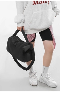 Detail of a black quilted puffer bag featuring a decorative oversized side bow design