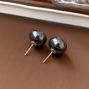 Macro shot of glossy black round pearl earrings with premium gold needle posts