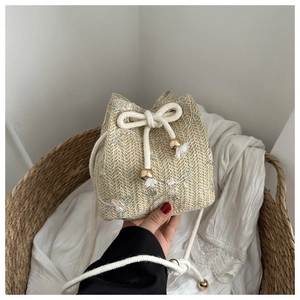 Close-up of beige woven bucket bag with floral embroidery and golden drawstring detail