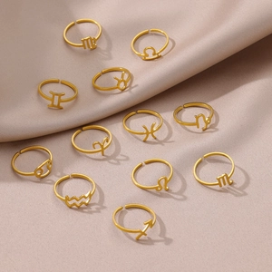Set of twelve gold-plated zodiac sign rings displayed on soft beige wrinkled fabric