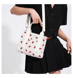Detail of white corduroy shoulder bag with red strawberry pattern and removable strap