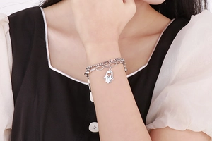 Double-layer silver chain bracelet with Hamsa Hand pendant on a woman's wrist