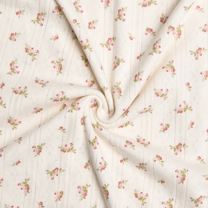 Detail of off-white knit cotton fabric with red and green floral pattern and textures