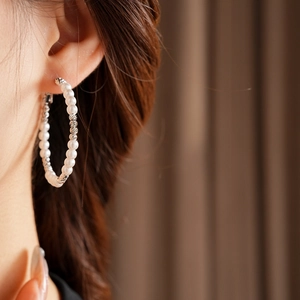 Close-up of a model wearing large silver beaded hoop earrings with white pearls
