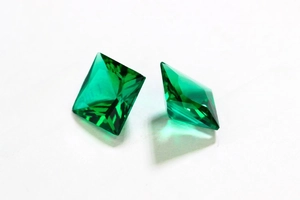 Macro shot of two deep green emerald-cut gemstones on a clean white background